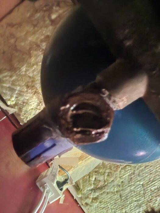 Närbild på en del av en vattenpump där det syns en läcka vid en anslutning, med en blå skålformad del och ett elektriskt uttag i bakgrunden.