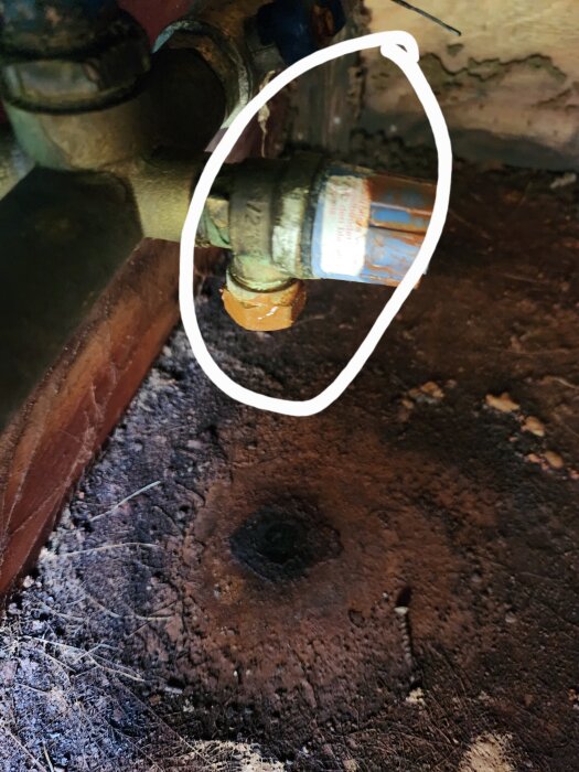 Markerad del av en gammal ventil eller röranslutning i behov av byte, omgiven av rost och smuts.