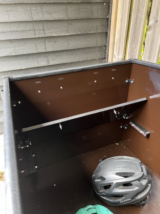 Förvaringslåda inomhus, med hjälm i botten, mot en träpanelvägg.