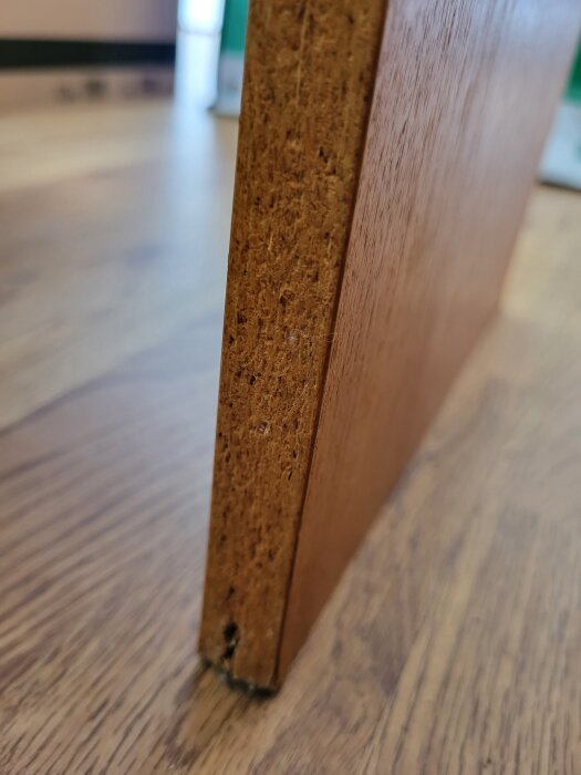 Närbild av kanten på en bokhylla eller skiva i trä, som visar sprickor i materialet.