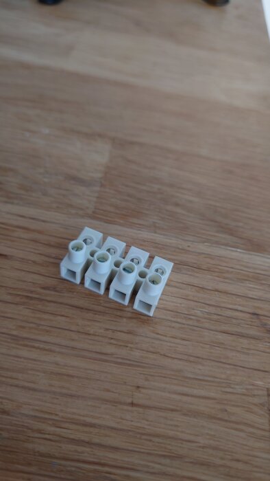 Vit kopplingsplint för PAX Passad fläkt, med öppningar för trådar på en sida och hål på ovansidan för fläktmotordelen, placerad på träyta.