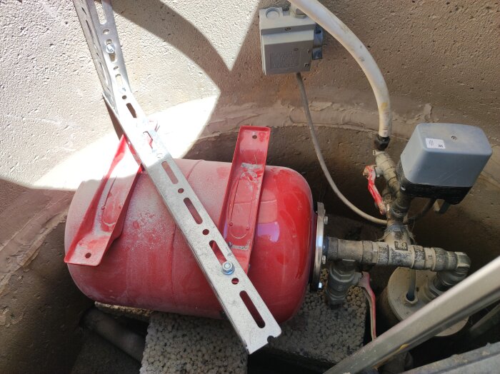 Röd hydropress installeras upp och ner i en brunn, fäst med metallstag, omgiven av rör och elektriska komponenter.
