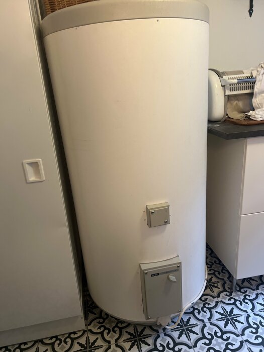 En vit varmvattenberedare av märket NIBE, modell ES20-300-1, står i ett kök med mönstrat golv.