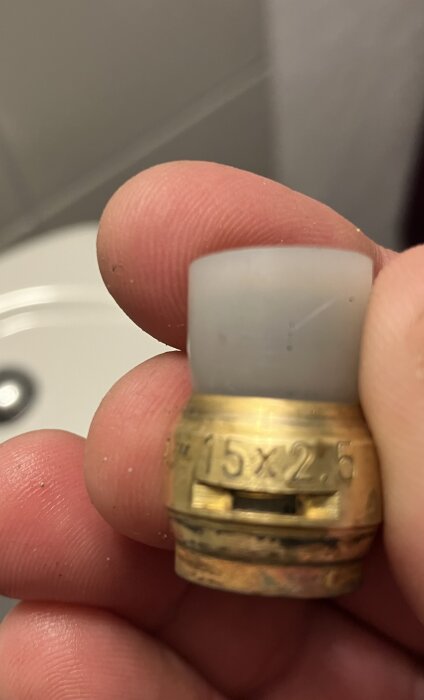 Närbild av en koppling till en kulventil, hålls mellan fingrar, med ingraverad text "15x2.5".
