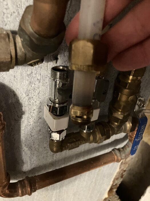 Kulventilinstallation med flera rörkopplingar och droppande mutter, handen håller PEX-rör med klämring mot kulventilen.