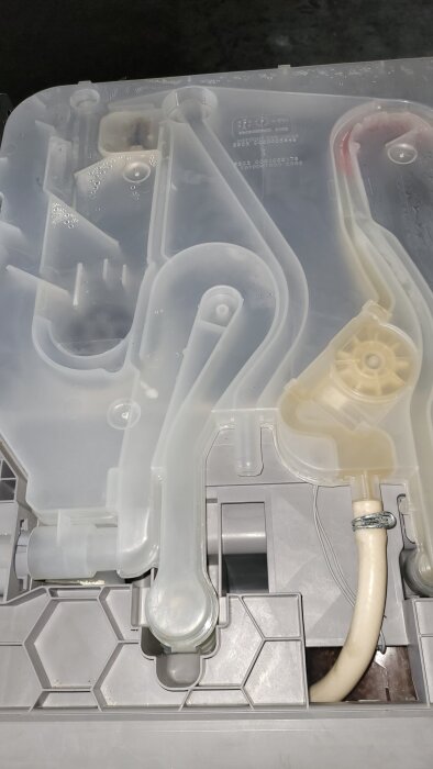 Grå plastgenomföring i påfyllningskassett med anslutna rör och mekaniska delar.