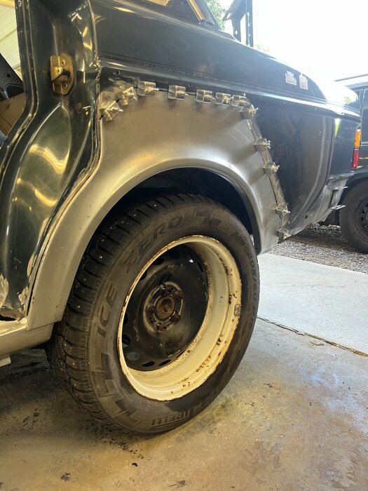 Bilens bakre hjulhus med klämmor och anpassad plåt för pågående karosserireparation i garage.