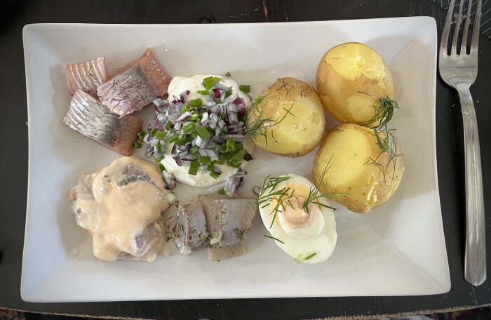 Silltallrik med ägghalvor, gräslök, rödlök, potatis och olika sorters sill inklusive Brantevikssill och Kalleskaviar-sill.