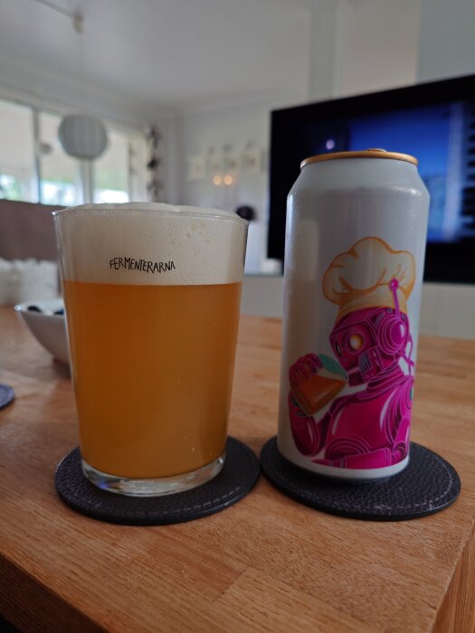 Ett glas öl från "Fermenterarna" med en burk bredvid med motiv av en robot med bagarmössa.