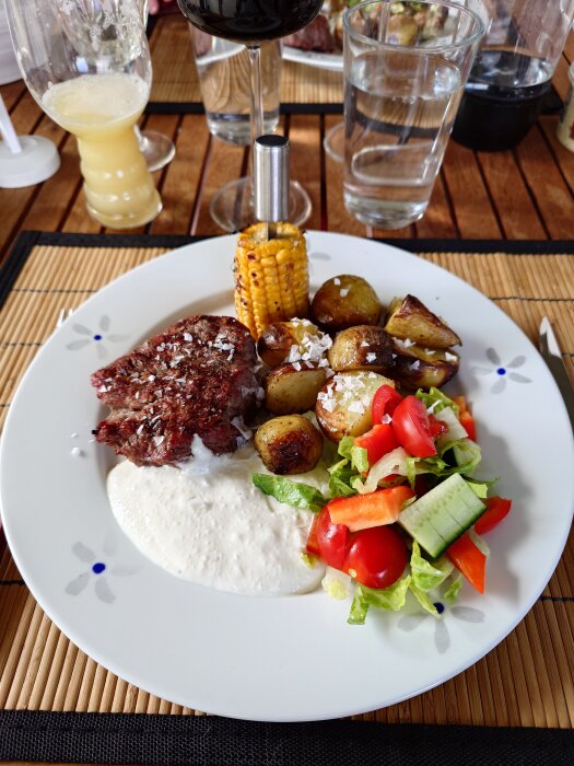 Grillad oxfilé, ugnsbakad potatis, grillad majs och getostsås på en tallrik med sallad.
