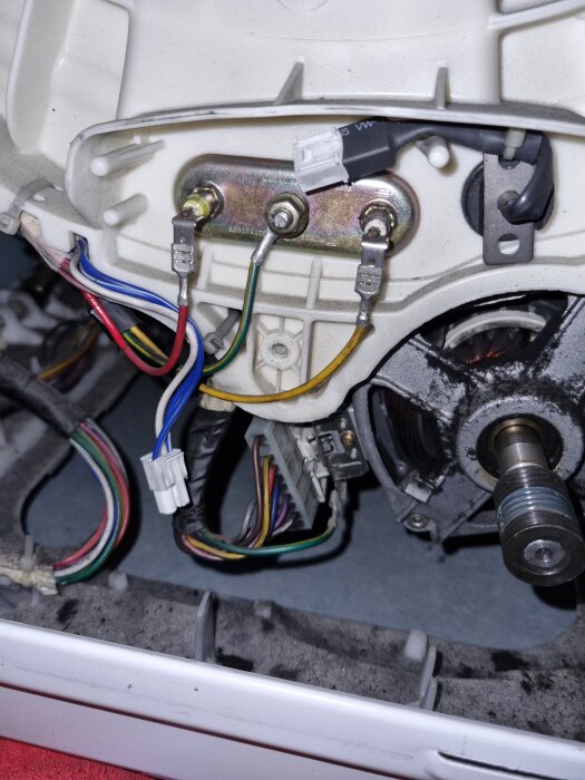 Närbild av insidan av en tvättmaskin med synliga ledningar och motor, potentiellt relaterad till ett problem med en snurrande trumma.