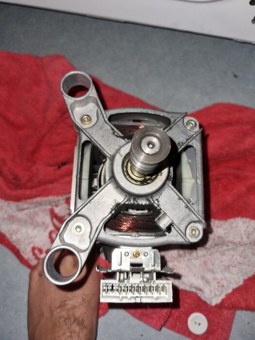 Motor från tvättmaskin med synliga kopparlindningar, placerad på en röd handduk.