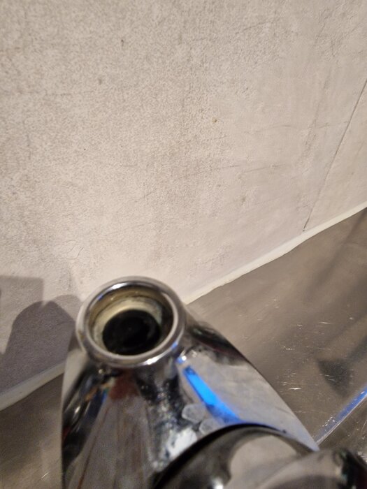 Bruten pipnippel på ett vattenkran med metallisk yta mot en ljus bakgrund.