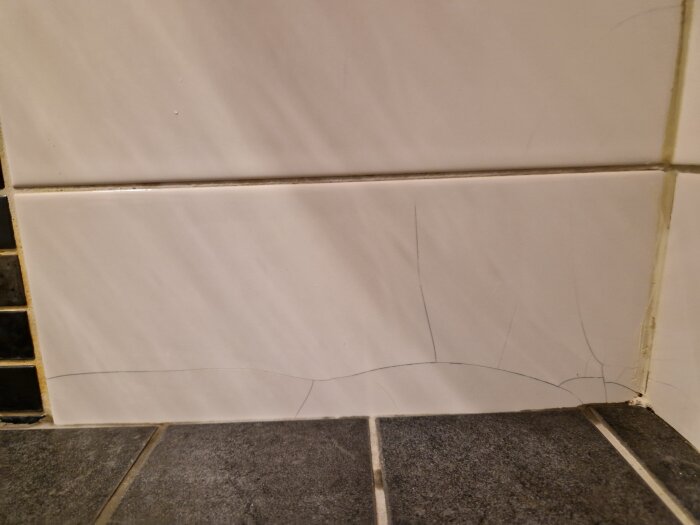Tunna sprickor i vit kakelplatta i dusch, möjligen orsakade av ålder. Badrummet är minst 10 år gammalt.