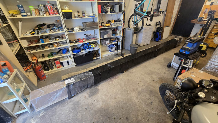 Svart, lång förpackning med markismaterial samt verktyg och hyllor med diverse renoveringsutrustning i ett garage.