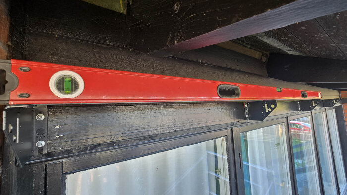 Rött vattenpass på svart trälist ovanför fönster med monterade konsoler för markiser.