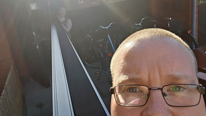 Närbild på en person framför en lång markisprofil, omgiven av cyklar och skugga.