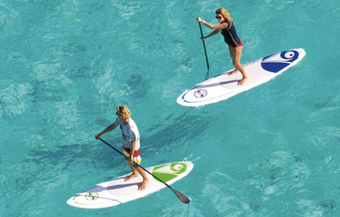 Personer paddlar på stand up paddleboards på klart blått vatten.