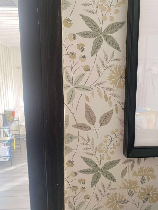 Tapet med grönt och gult bladmönster vid en mörk dörrkarm i kök.