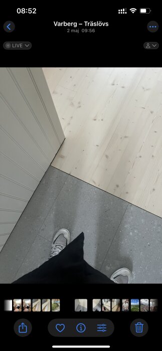 Övergång mellan ljus trägolv och grått klinkergolv vid dörröppning, synlig sko på det grå golvet.