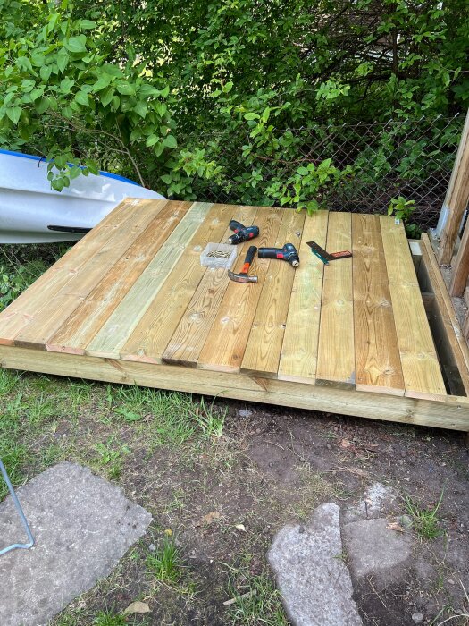 Upptäcktsprocess av att bygga en trätrall, med verktyg som skruvdragare och hammare. Grönska och staket syns i bakgrunden.