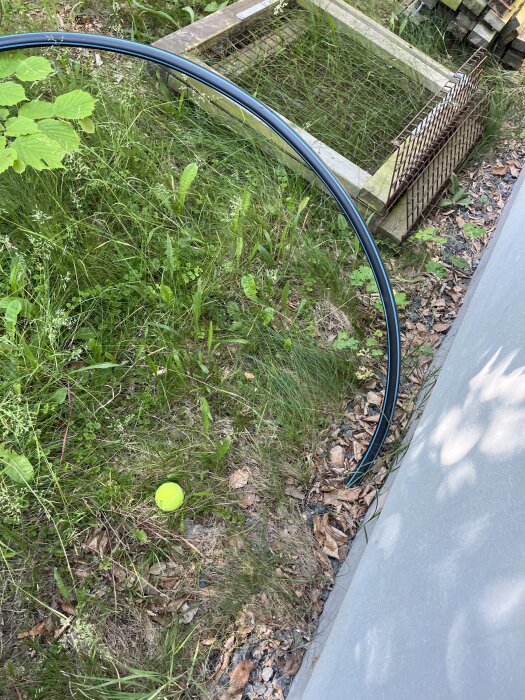 Blå PEM-slang sticker upp ur marken vid husets kortsida, omgiven av gräs och löv, med en gul tennisboll nära.