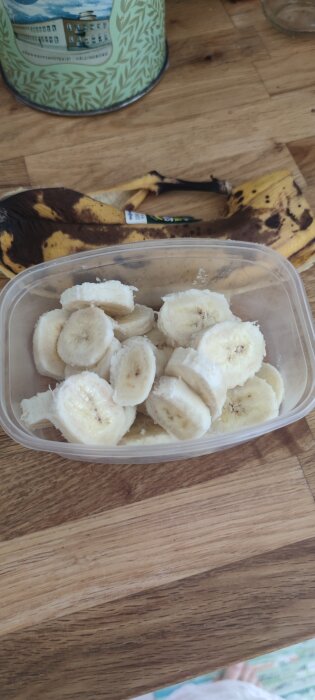 Frysta bananskivor i plastbehållare på träbord, redo för hemmagjord bananglass med kakao och honung.