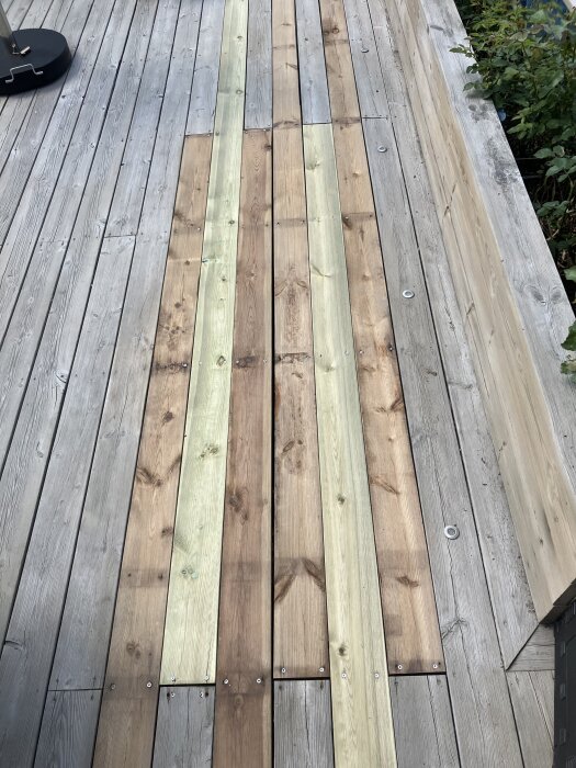 Fyra nyare och ljusare träplankor installerade mitt i en äldre, grånad altan.