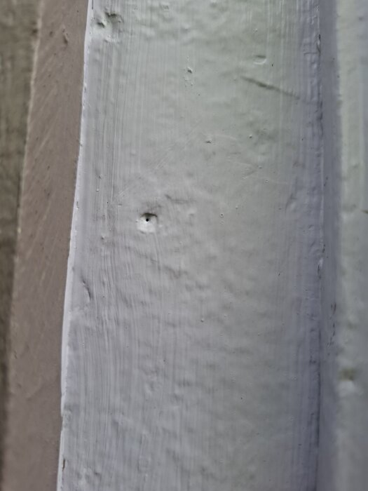 Närbild av en målad vägg med synliga små hål och ojämnheter i ytan.