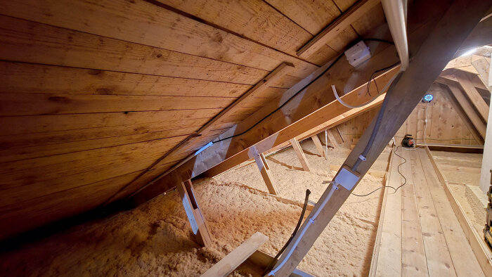 Vind med isolering och träramar, synliga VP-rör och ventiler som förberetts för ventilationssystem; kablar klamrade längs takstolarna.