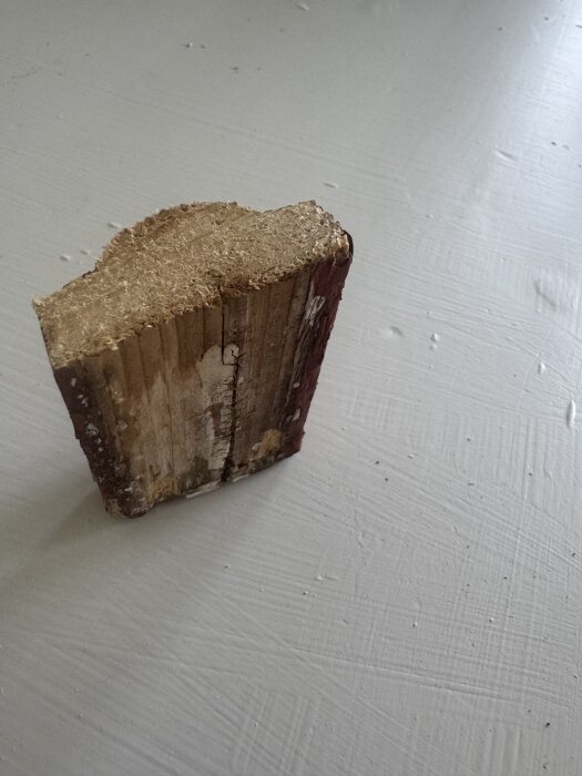 En bit av en vindskiva med avskalad färg och tecken på röta stående på en ljus yta.