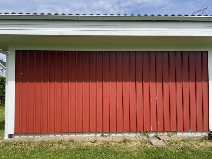Röd träfasad av en husvägg från 90-talet, med vitmålade vindskivor och betonggrund. Skuggor från taket på fasaden.