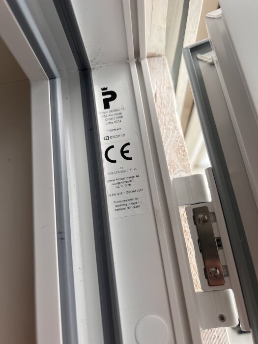 Närbild av altandörrens gångjärn med etiketter och CE-märkning synliga.