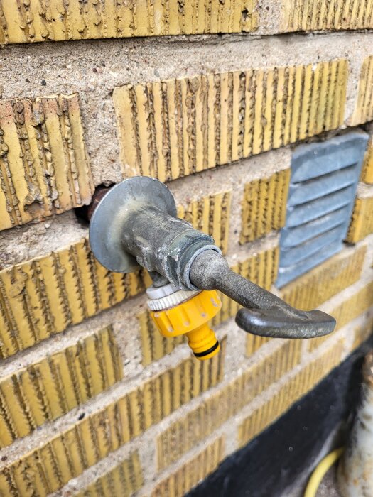 Utvändigt kranhus i metall med gul anslutning på en gul tegelvägg.