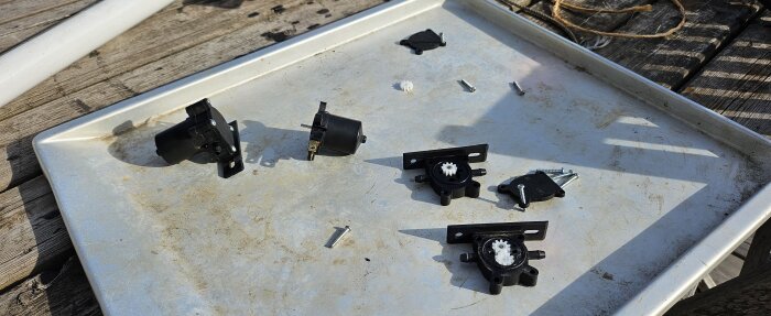 Svarta plastdelar och skruvar på ett metallbricka, förmodligen delar till en spolarpump.