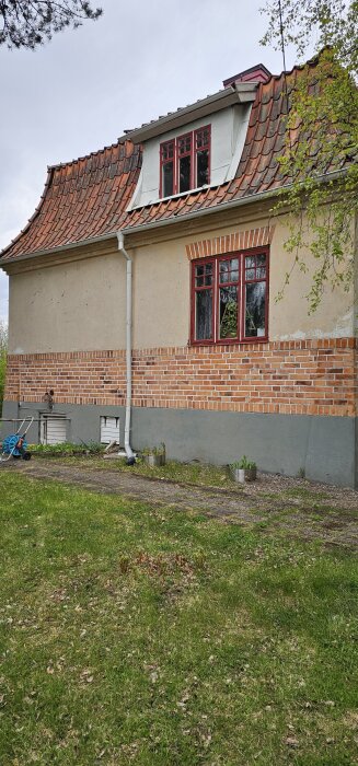 Tegelhus med rött tegeltak och fönster, avbildat från sidan med trädgård och gräs i förgrunden.