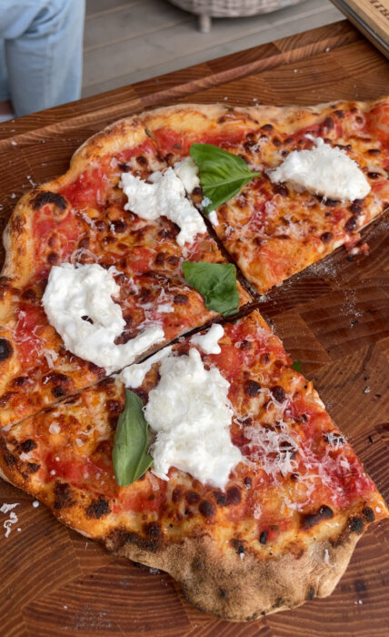 Pizza med tomatsås, mozzarella och färska basilikablad på ett trähuggebord, lätt bränd kant.