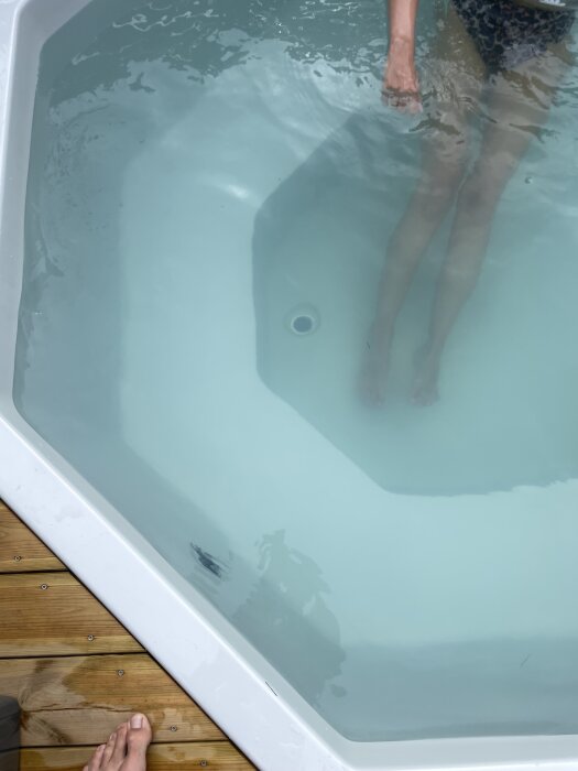 Grumligt vatten i en terrasspool med en person som står i vattnet och synliga träplankor vid poolkanten.