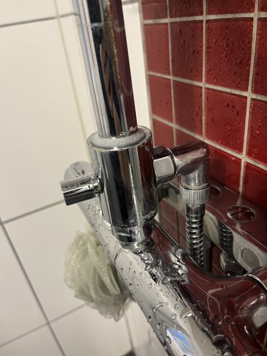 Duschblandare med läckage, vatten droppar från en ventil mot en röd kakelvägg. Fråga om reparation eller utbyte.