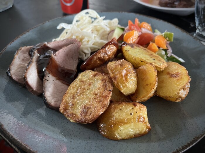 Grillad pluma med rödvinssås, ugnstekt potatis, sallad och coleslaw på en tallrik.