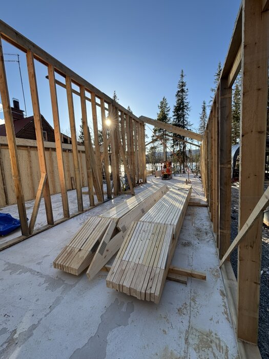 Trästomme för byggnad under uppförande, med liggande plankor på marken och en klar himmel i bakgrunden.