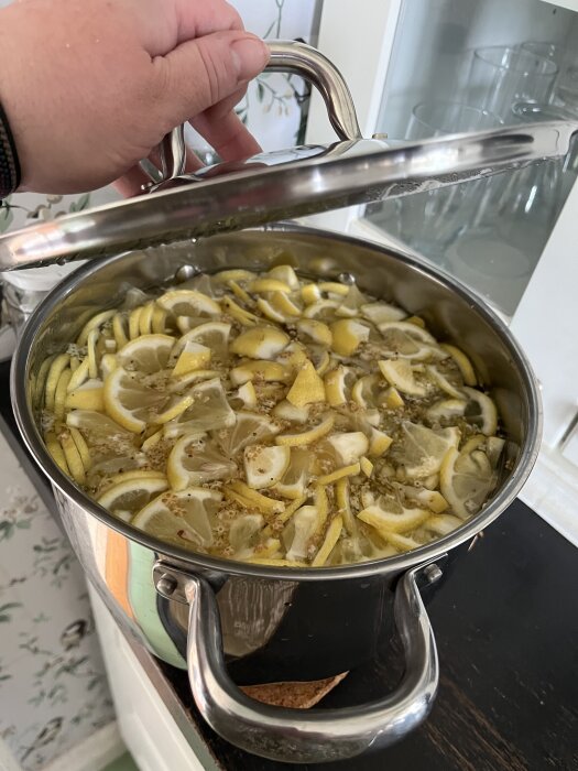 En gryta med citronskivor och kryddor, locket lyfts av en hand.