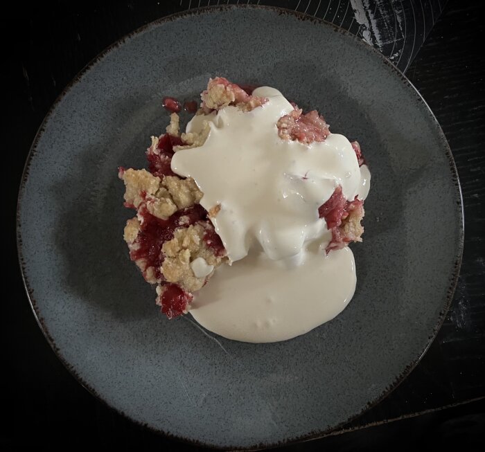 Jordgubbspaj med smultopp serverad med vaniljsås på en mörk tallrik.