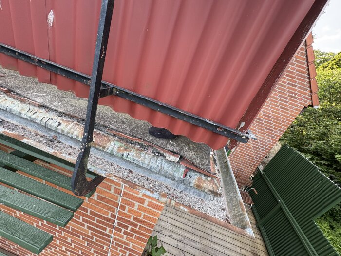 Tak med röd plåt, betong och gamla takpapp på en tillbyggnad från 60-talet. Inlägget handlar om att renovera och lägga ny takpapp.
