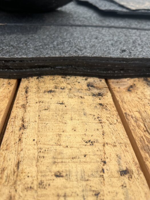 Närbild av fyra lager takmaterial ovanpå torrt råspånt, avslöjat efter att ha tagit hål i konstruktionen.