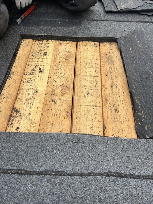 Råspont av trä under avlägsnat takmaterial, avslöjar lagerstruktur i taket.