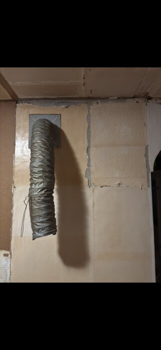 Vägg mellan kök och vardagsrum med murstock och ventilationsrör, potentiellt innehållande asbest i beklädnaden.