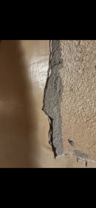 Murad vägg med synligt lager av grovt puts, potentiellt asbesthaltig, mellan kök och vardagsrum i hus byggt 1967.