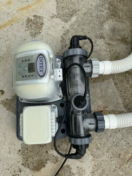 Pump- och filtersystem på sliten yta, Intex varumärke synligt. Kopplingar och kablar anslutna, möjligtvis problem med felmeddelande eller flöde.