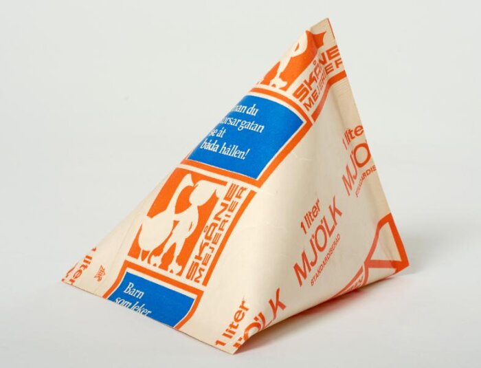 Treformad mjölkförpackning från 60-talet med orange och blå text och bilder. Märkt som 1 liter av märket Skåne mejerier.